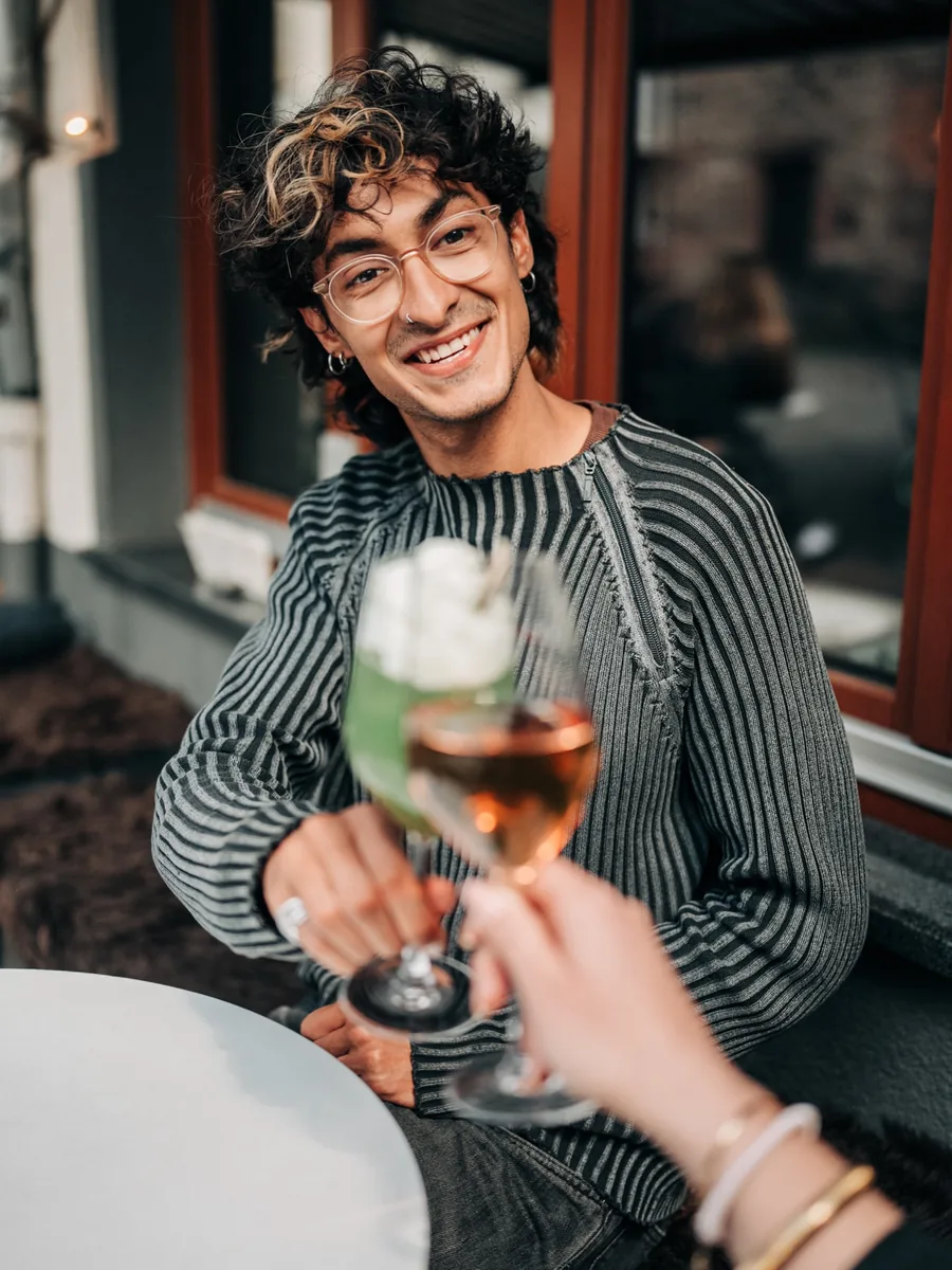 Zwei Gäste stoßen an der Außenbestuhlung mit Rosé und einem grünen Drink an