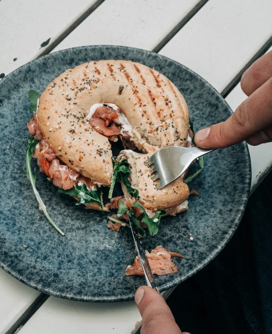 Aufgeschnittener Bagel mit Lachs, Frischkäse und Rucola auf blauem Teller