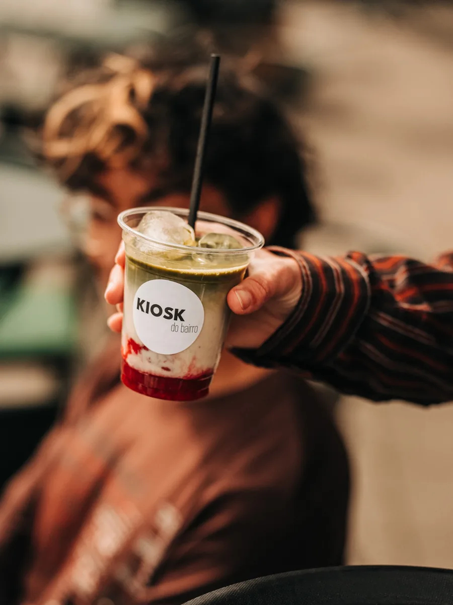 Becher mit rundem KIOSK-do-bairro-Aufkleber, gefüllt mit Matcha und Beerenpüree