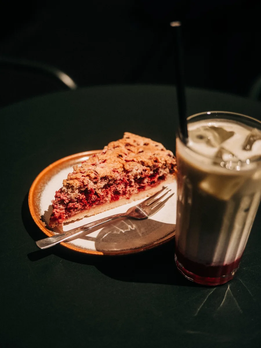 Ein Stück Himbeer-Streuselkuchen neben einem Eiskaffee mit Beerenspiegel