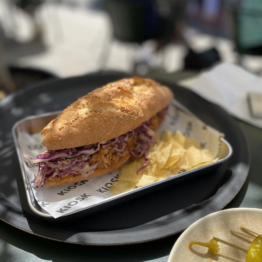Sandwich mit Pulled Pork und Rotkohl auf KIOSK-Papier, dazu Kartoffelchips